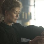 Rosamund Pike pours a beaker into a funnel as Marie Curie in the movie Radioactive