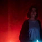 Surrounded by red fog in the woods, Alison Brie holds her phone's flashlight in the movie The Rental