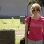 Gillian Wallace Horvat wears green sunglasses and a pink Hollywood shirt at a cemetary in the film I Blame Society