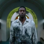 Yahya Abdul-Mateen II stands in a hallway wearing dirty clothes and looking creepily at the camera in the movie Candyman