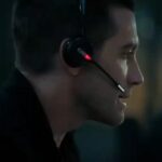 Jake Gyllenhaal faces his computer with a wireless phone headset on in the movie The Guilty