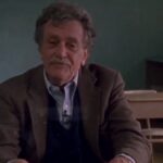 Kurt Vonnegut stting at a teacher's desk in a classroom in the documentary Kurt Vonnegut: Unstuck in Time