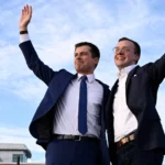 Pete Buttigieg and his husband Chasten stand with their arms around each other waving