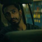 Riz Ahmed sits in a dark car looking out in the movie Encounter