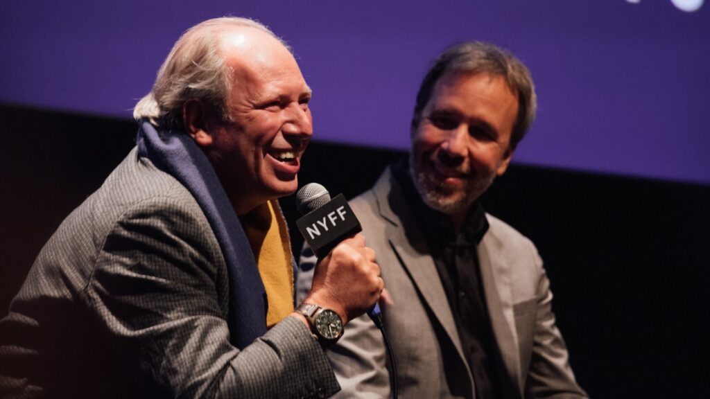 Hans Zimmer sits next to Denis Villeneuve holding a microphone and talking about the movie Dune at a NYFF Q&A