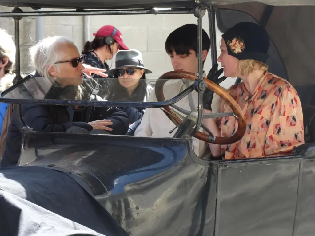 Kristen Dunst and Kodi Smit-McPhee sit in an old car while director Jane Campion talks to them