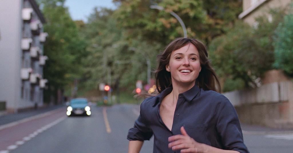 Renate Reinsve looks happy as she runs down a busy road in the movie The Worst Person in the World