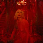 Carlson Young stands in an empty room bathed in red light in the movie The Blazing World