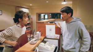 A man and woman stand on opposite sides of a counter at a restaurant staring each other down in the film Beyond the Infinite Two Minutes