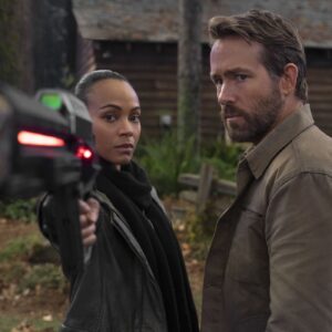 Zoe Saldana stands next to Ryan Reynolds pointing a futuristic gun at something in the movie The Adam Project