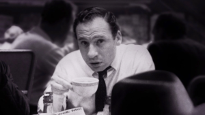 A black and white still of Mel Brooks as a young man drinking coffee at an Automat restaurant in the documentary The Automat