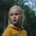 A little blond girl in a yellow jacket looks frightened in the Norwegian movie The Innocents