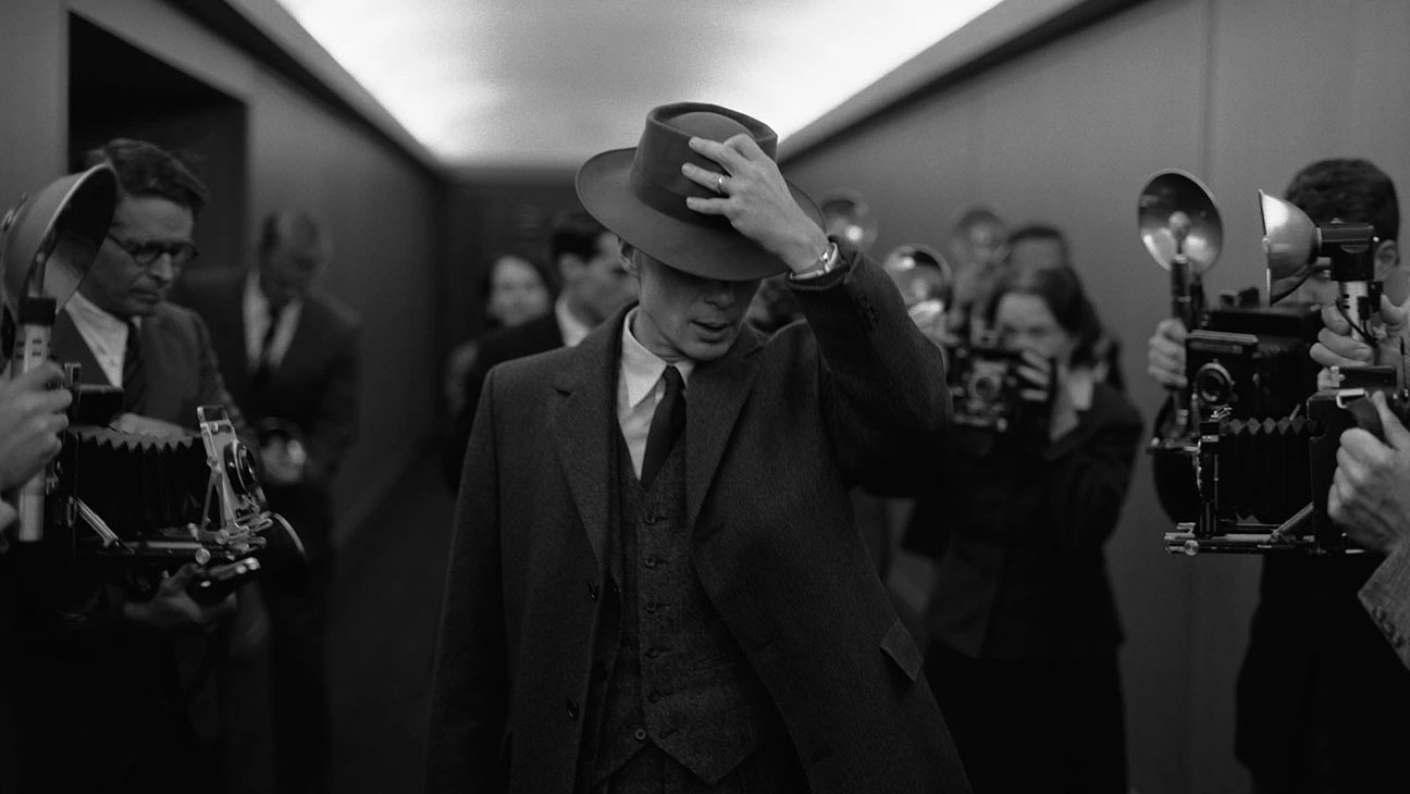 Cillian Murphy tips his hat to reporters in a black and white screenshot from the movie Oppenheimer.