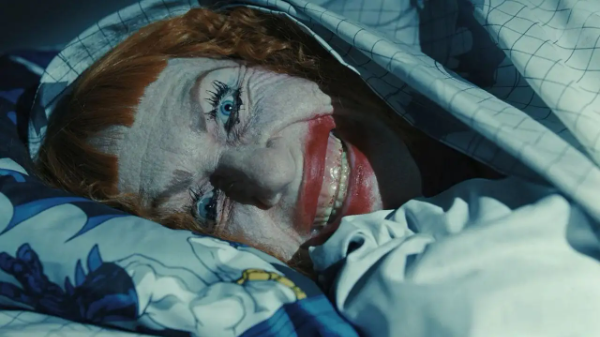 Amy Madigan peeks out from covers with an unhinged smile on her face in the film Weapons.