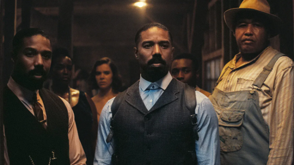Michael B. Jordan's two characters stand next to each other and in front of other characters in the film Sinners.